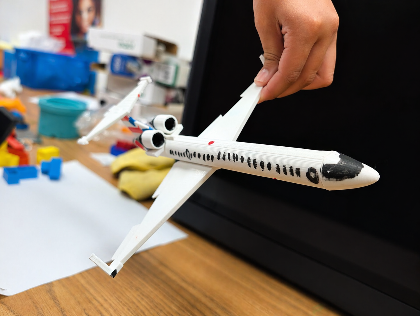 Student holding a large white 3D printed airplane with drawn window details and attached wings.