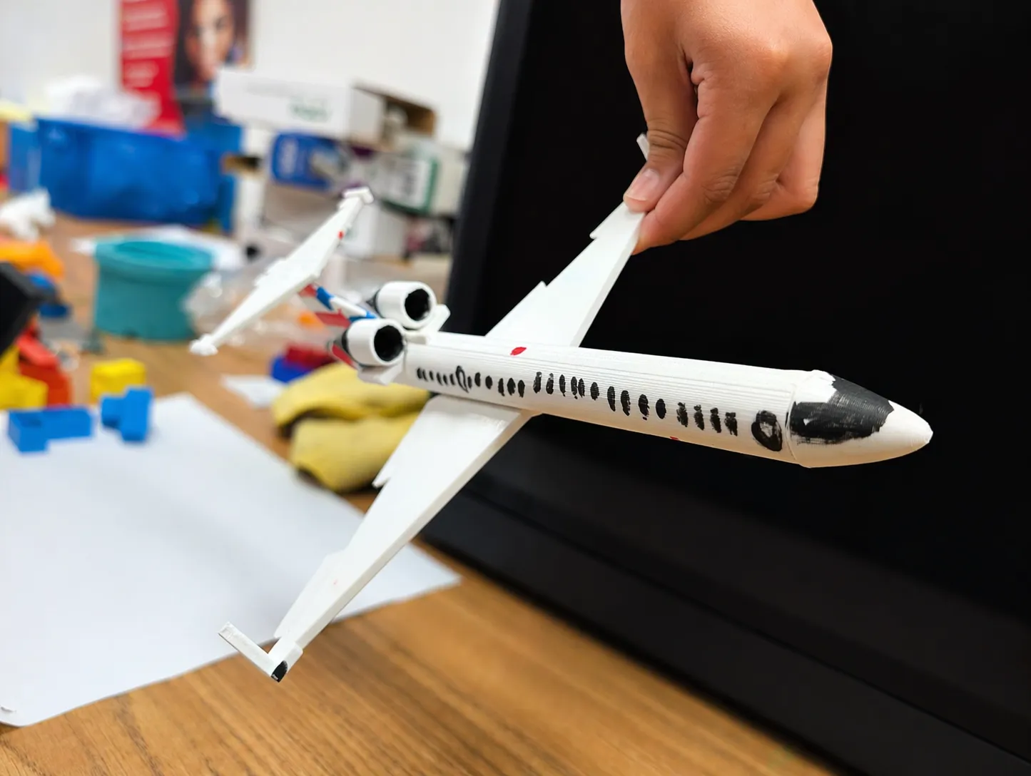 Student holding a large white 3D printed airplane with drawn window details and attached wings.